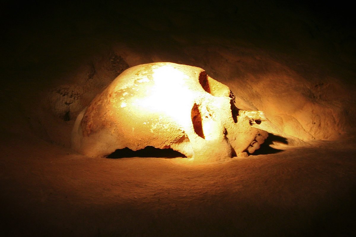 Actun Tunichil Muknal A skull illuminated by a warm light against a dark background.