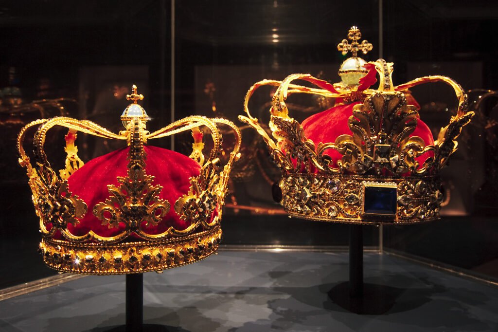 Two ornate gold crowns with red velvet interiors displayed in a museum setting.