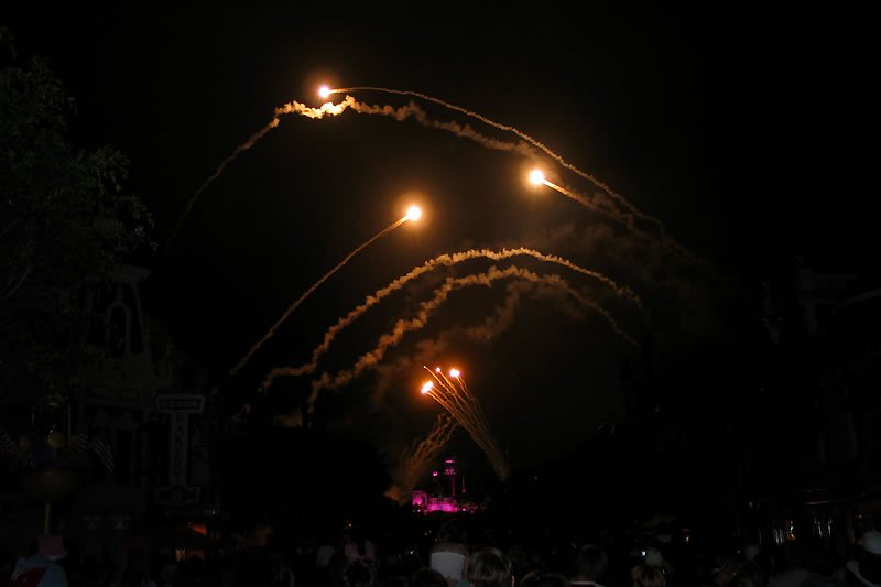 Golden fireworks trace paths across the night sky, igniting with bursts of light over a dark landscape.