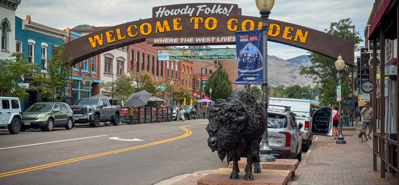 Golden, Colorado A picturesque street in Golden, Colorado, featuring a welcoming sign and a prominent bison statue. The scene is set against a backdrop of historic buildings and mountains.