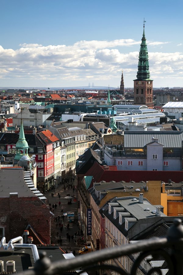 A panoramic shot showcasing historic architecture with prominent green-topped spires amidst a dense urban landscape under a partly cloudy sky.