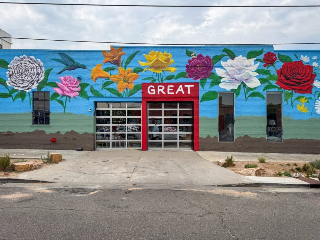 A vibrant mural on a building wall featuring large colorful flowers and a hummingbird against a blue sky.