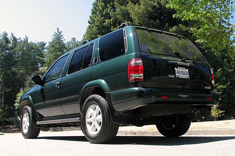 A green SUV is shown from multiple angles, nestled amongst dense green trees on a sunny day.
