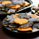 Halloween A plate of Halloween-themed cookies with orange and black icing displayed on a dark wooden table.