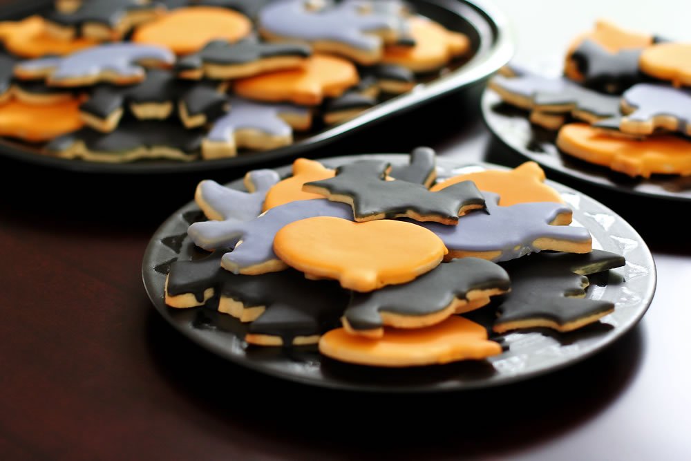 A plate of Halloween-themed cookies with orange and black icing displayed on a dark wooden table.