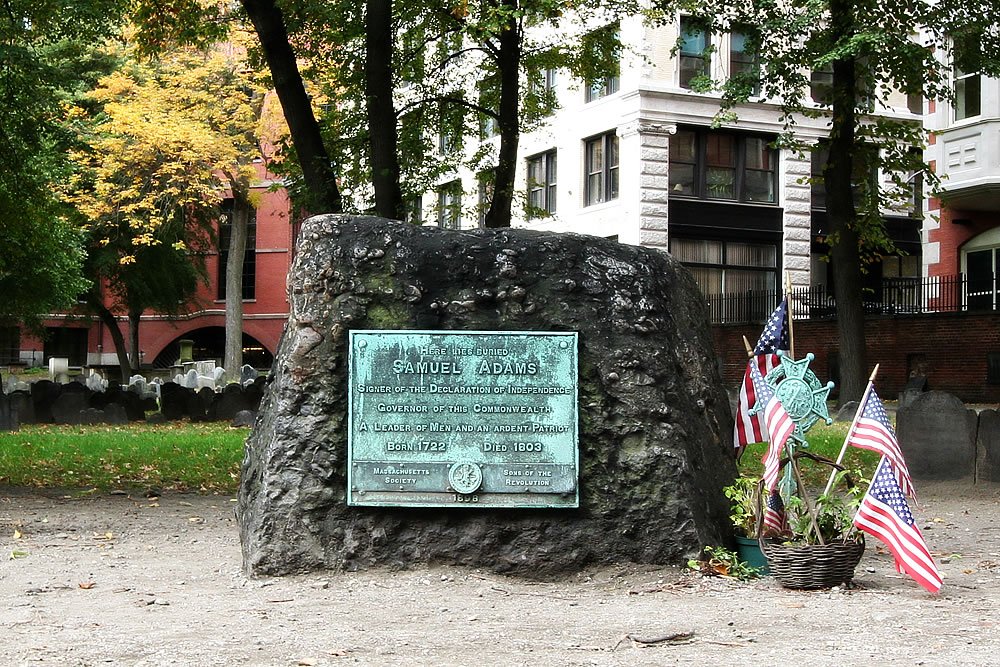 A historical marker plaque on a stone monument commemorating Henry Hudson, adorned with American flags.