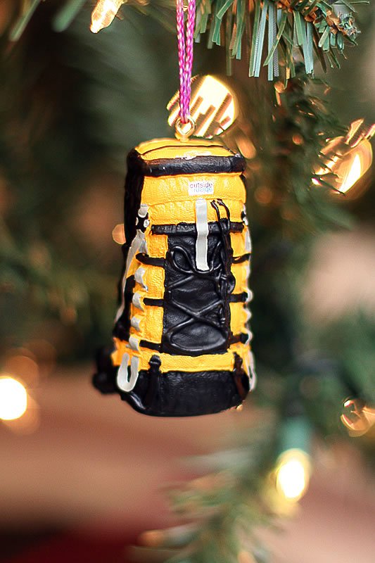 A close-up of a yellow and black hiking backpack hanging as a Christmas ornament on a tree.