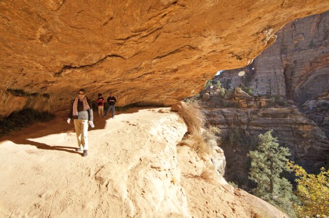 Tourists walking along a sandy trail to Mesa Arch in the Utah desert.