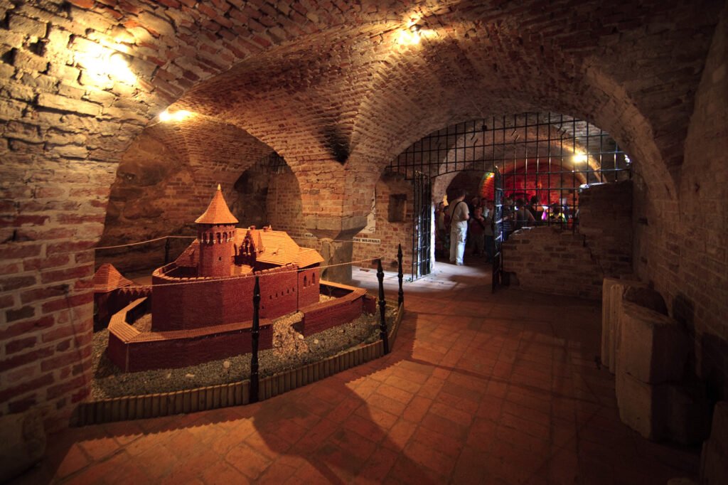 A dimly lit, brick-arched hallway leading to a castle model display.