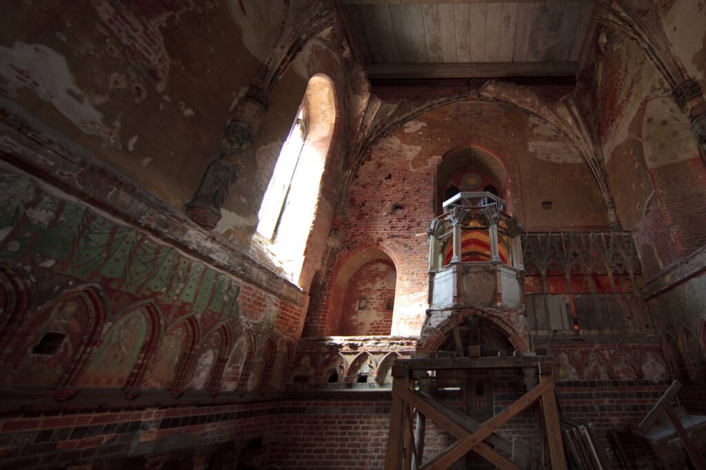 An interior view of an ancient building featuring faded frescoes and intricate architectural details.