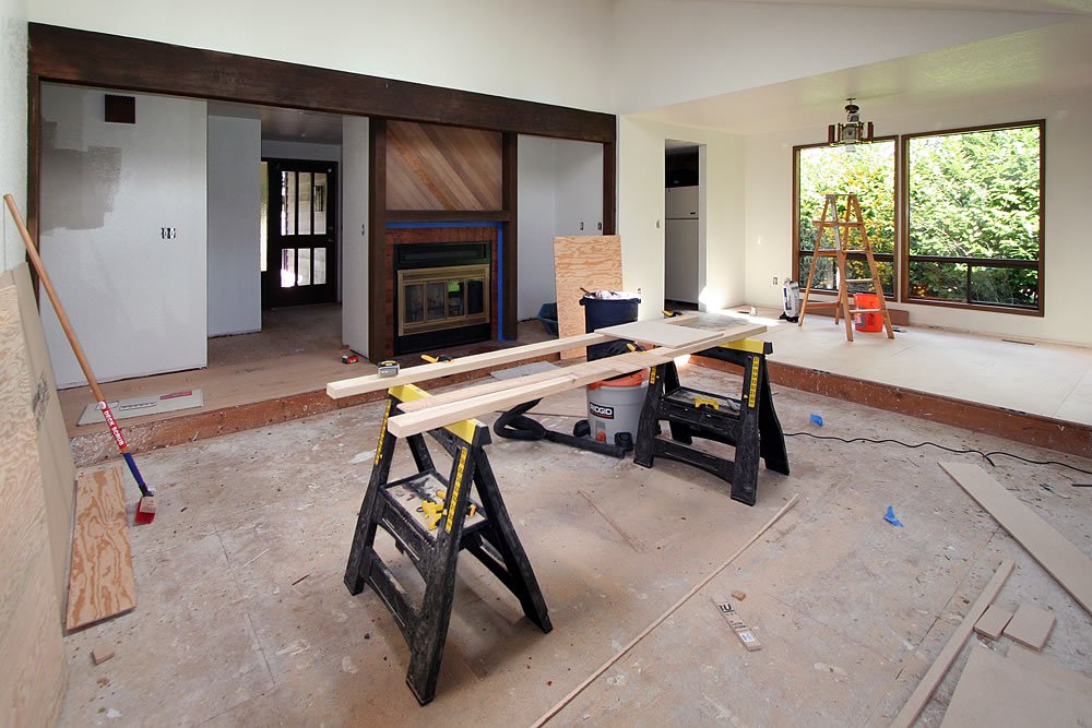 A room under renovation with tools and materials scattered around, looking out onto a lush green view.