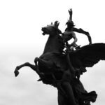 EIG Website A striking black-and-white silhouette of a statue featuring a horse and rider against a light sky background.