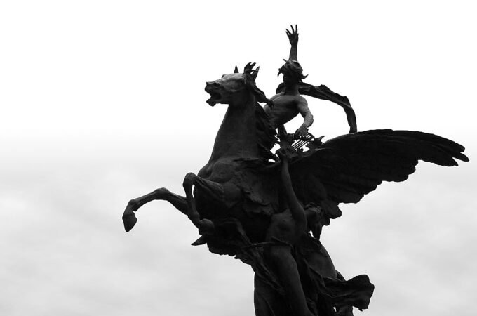 A striking black-and-white silhouette of a statue featuring a horse and rider against a light sky background.
