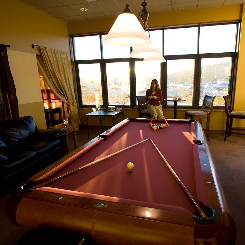 A woman sits by the window with a view of a city skyline, next to a purple pool table.
