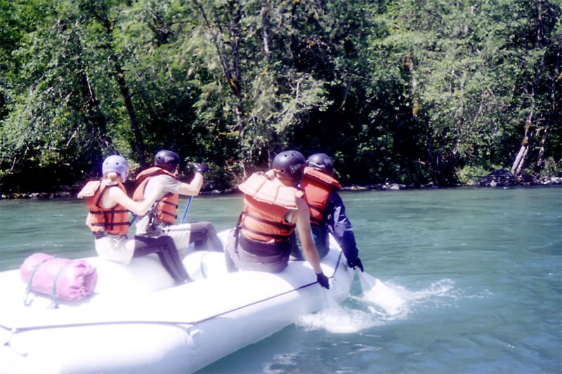 A group of people wearing life jackets enjoying a river ride in an inflatable boat.