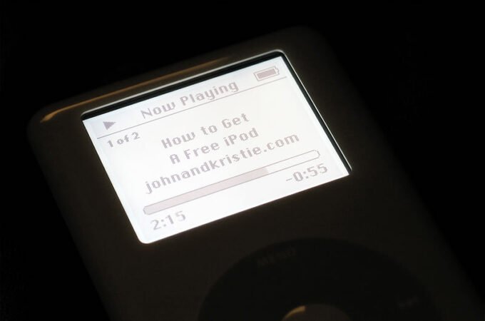 A close-up view of an iPod screen playing a podcast titled 'How to Get A Free iPod' from johnandkristie.com, highlighting the blog’s early tech and travel themes.