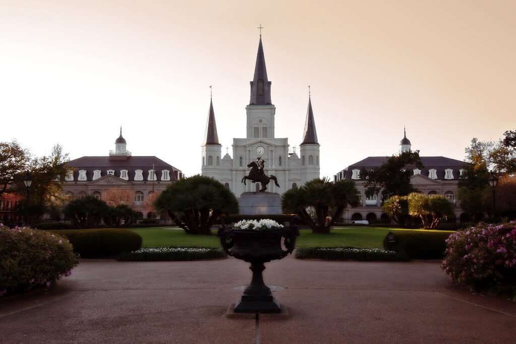 A twilight view of St. Louis Cathedral in Jackson Square, New Orleans, with the Andrew Jackson statue and ornate planters silhouetted against a glowing sky as John & Kristie enjoy a romantic evening stroll.