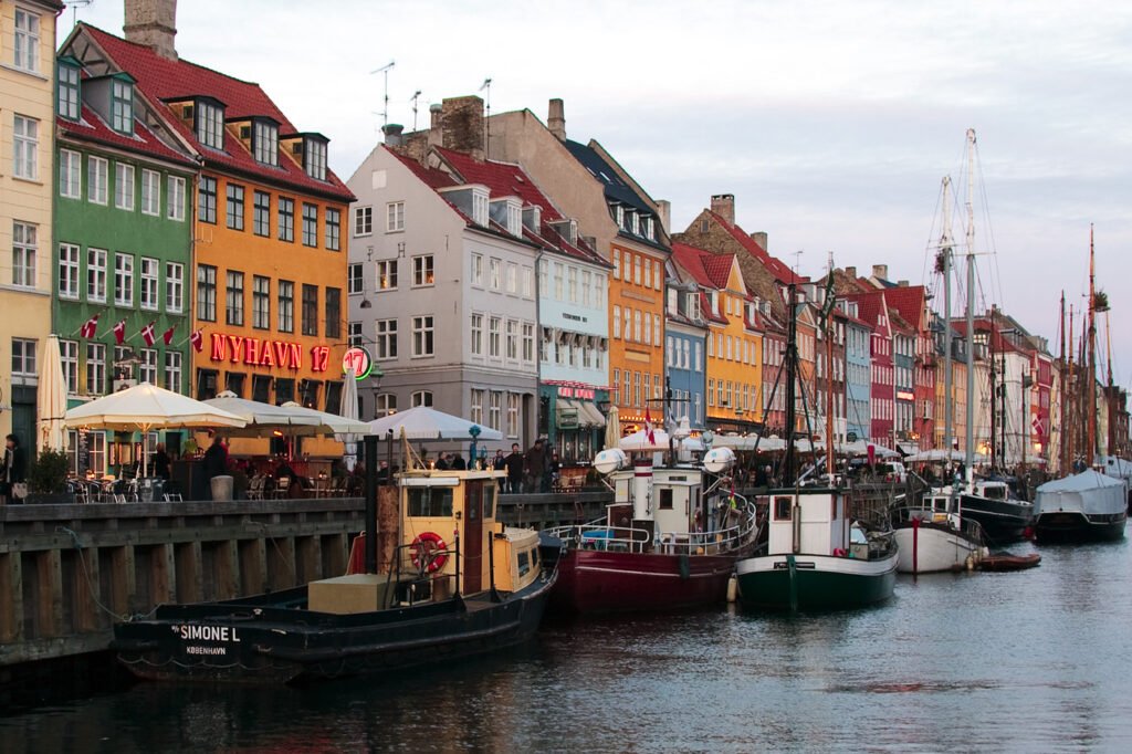 Vibrant, historic canal-side buildings in Copenhagen featuring a paddle steamer boat docked by a pier.