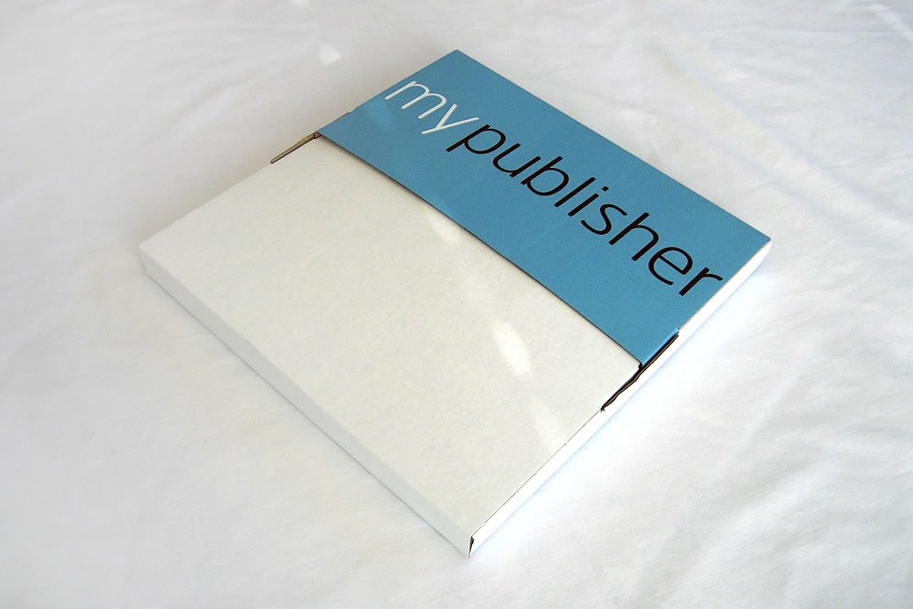 A white book with a blue Mypublisher label lies on a white bed sheet.