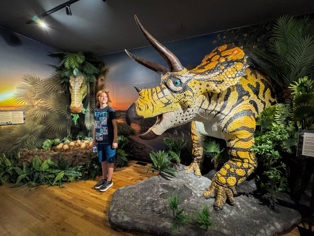 A photo of John and Kristie experiencing a Brontosaurus exhibit with vibrant colors and prehistoric decor.