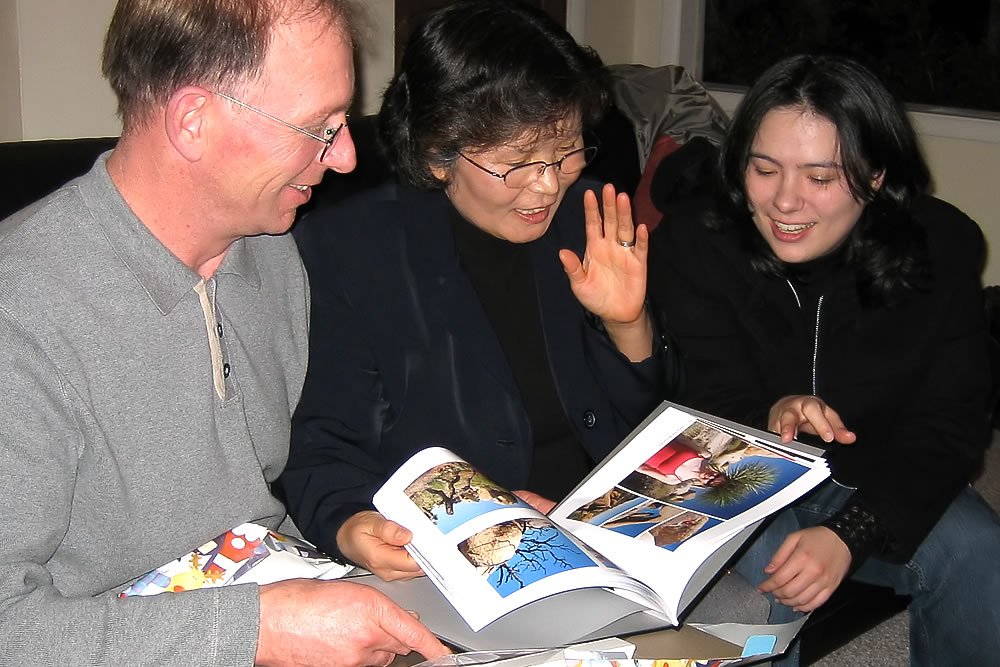 Three people casually browsing through a book or magazine together indoors. They are engaged with the content, appearing to enjoy the moment.
