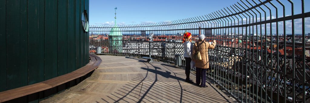 John and Kristie stand by a railing looking out over a sprawling cityscape on a sunny day.