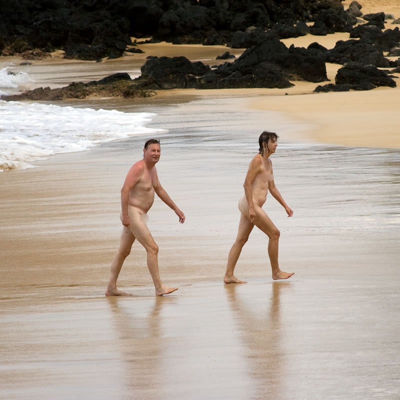 Two individuals enjoy a leisurely walk along the wet sand of a serene beach.