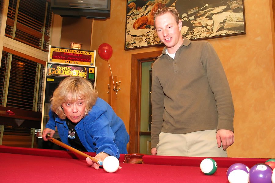 John and Kristie enjoy a game of pool. Kristie focuses intently on her next shot while John watches.