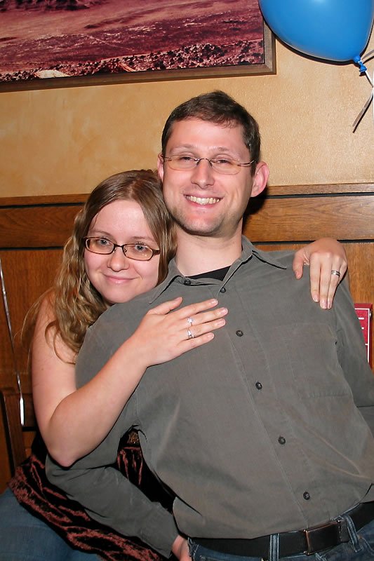 John and Kristie are posing together warmly indoors with a blue balloon in the background, celebrating together.