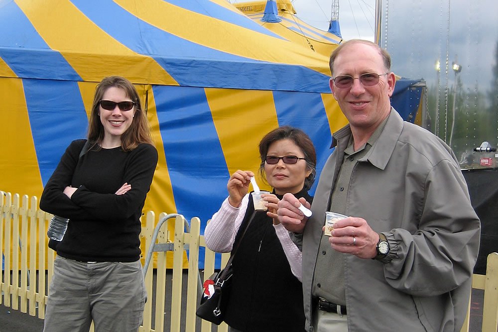 John and Kristie enjoying a day out at a carnival, standing in front of a colorful tent.
