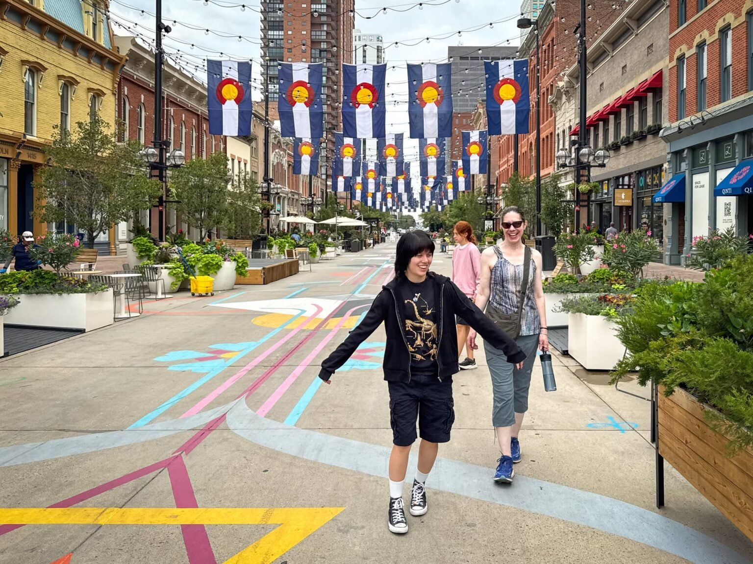 John and Kristie are walking down a colorful pedestrian street lined with banners. They seem to be enjoying their time exploring the city.