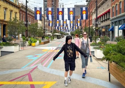 Denver Adventures John and Kristie are walking down a colorful pedestrian street lined with banners. They seem to be enjoying their time exploring the city.