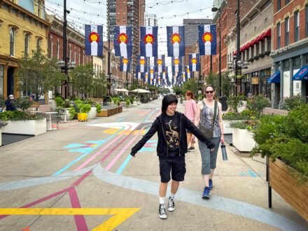 John and Kristie are walking down a colorful pedestrian street lined with banners. They seem to be enjoying their time exploring the city.