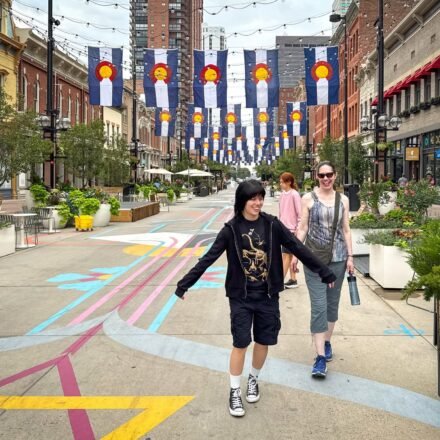 John and Kristie are walking down a colorful pedestrian street lined with banners. They seem to be enjoying their time exploring the city.