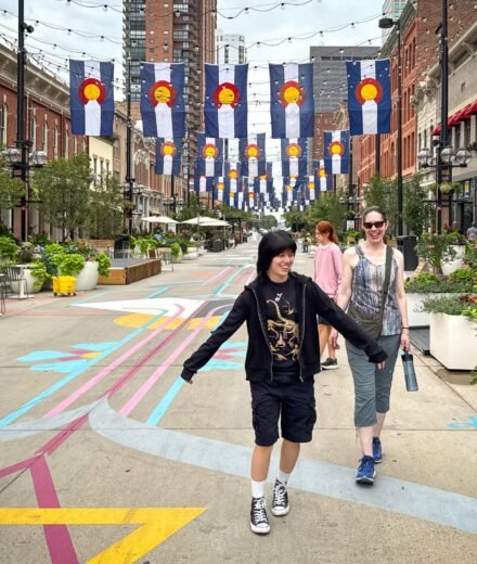 John and Kristie are walking down a colorful pedestrian street lined with banners. They seem to be enjoying their time exploring the city.