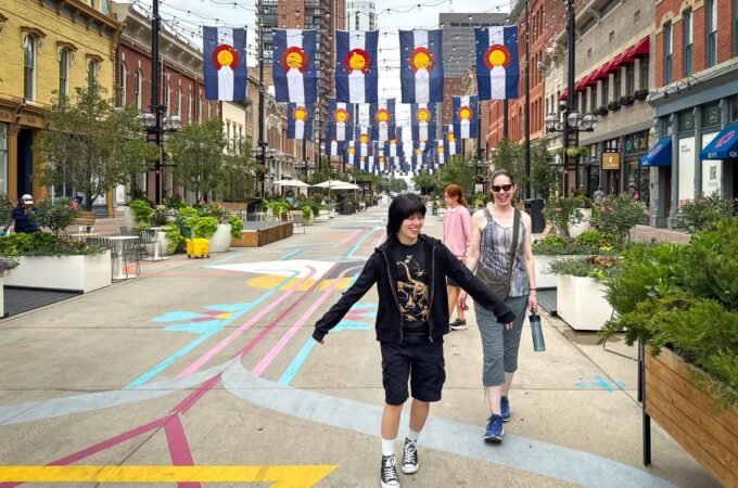 John and Kristie are walking down a colorful pedestrian street lined with banners. They seem to be enjoying their time exploring the city.