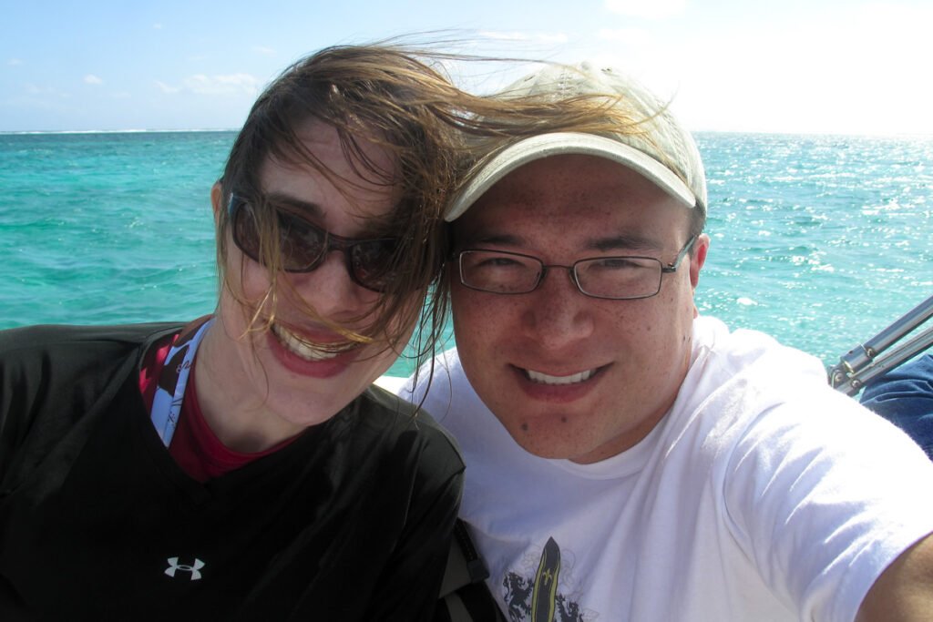 A cheerful selfie of John and Kristie on a boat with the turquoise ocean in the background.