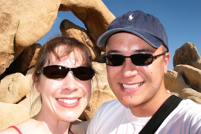 A close-up of John and Kristie smiling together under a clear blue sky with rocky formations in the background.