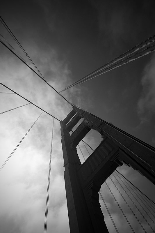 A dramatic black and white image captures the towering structure viewed from below, featuring prominent cable lines.