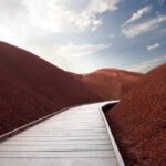 Front Yard Facelift A wooden walkway winds through vibrant red dunes under a blue sky with fluffy clouds.
