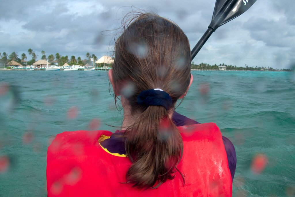 A person kayaking in clear blue waters with a tropical island in the background.
