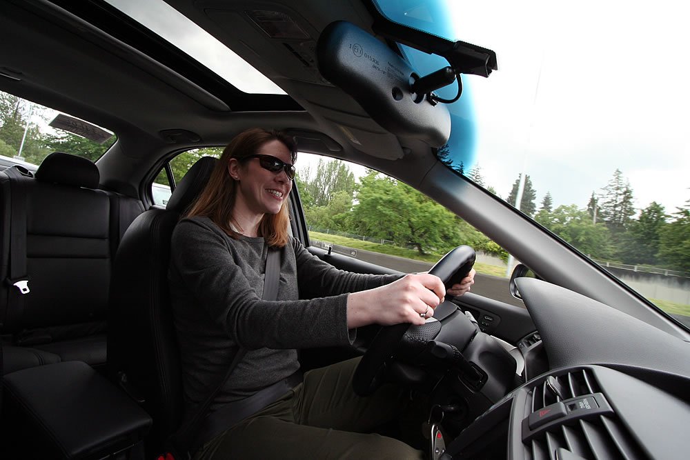 Kristie smiles while driving a car with a sunroof open, enjoying the green scenery of the Pacific Northwest.