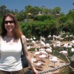 Kristie smiling in front of a flamingo exhibit with tropical trees in the background.
