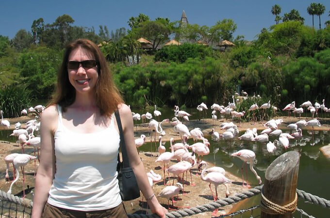 Kristie smiling in front of a flamingo exhibit with tropical trees in the background.