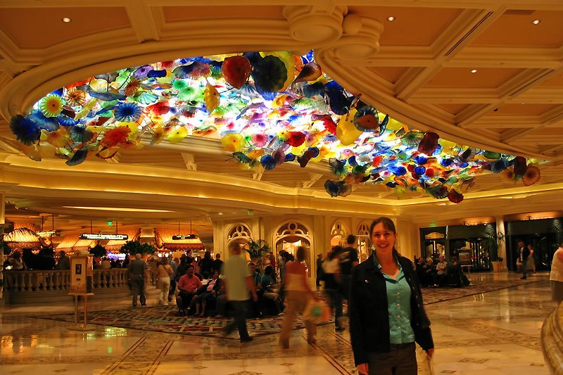 A woman smiles while standing in a luxurious lobby beneath a stunning, vibrant glass art installation.