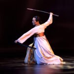 U2 at The Rose Bowl A dancer performs a graceful sword routine on stage wearing traditional white attire.