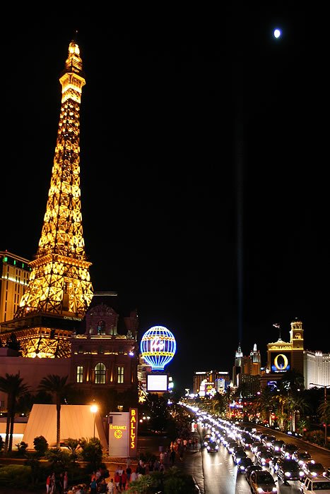 A night scene showcasing the iconic Paris Las Vegas Eiffel Tower illuminated with lights, adjacent to a busy road filled with moving cars.