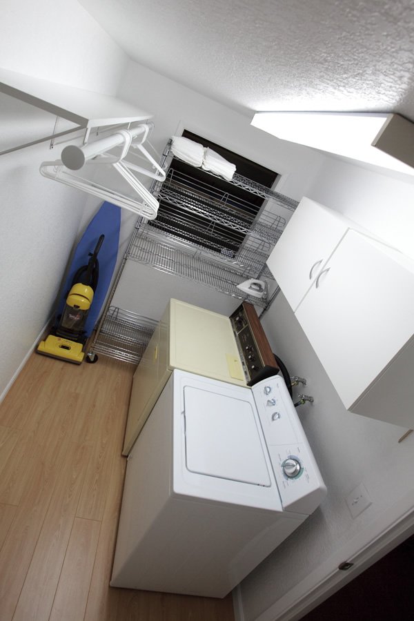 A compact laundry room featuring a white washer and dryer with a storage cabinet and a vacuum cleaner.
