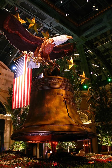 A close-up of the Liberty Bell surrounded by festive decorations. An American flag is visible in the background.