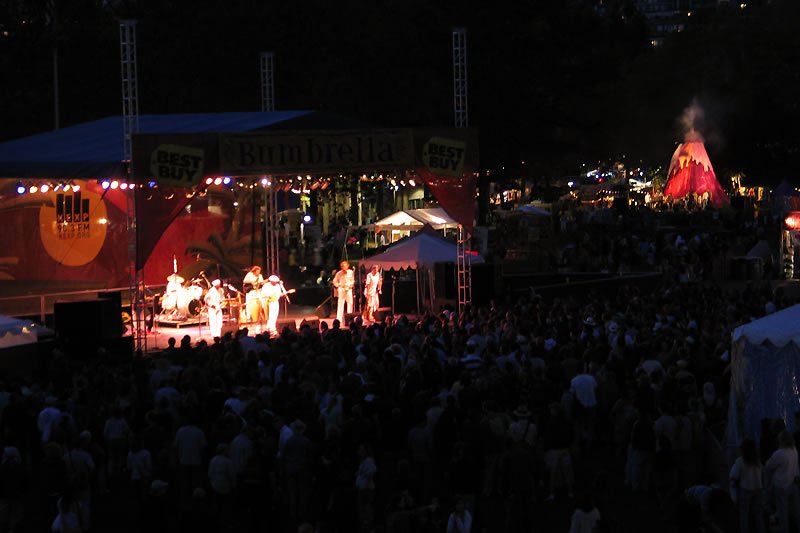 A band performs on stage under vibrant lights while a crowd gathers in front of them.
